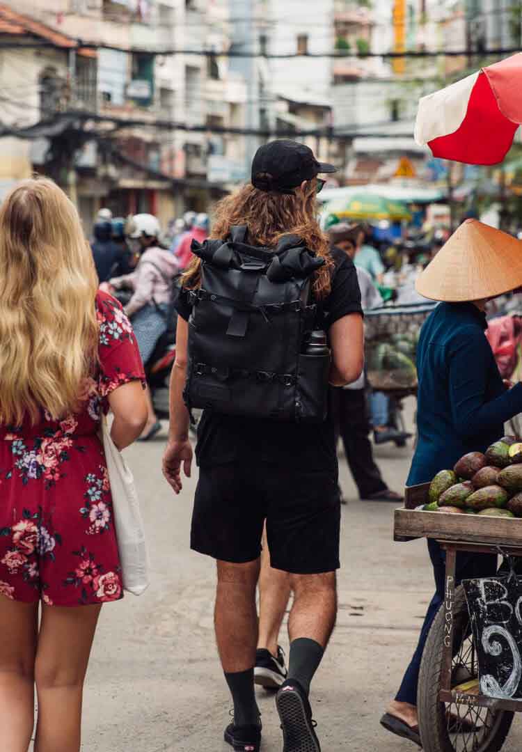 A person walks through a market wearing a PRVKE pack, in black.