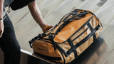 Man picking up the yellow 60L Carryall Duffel 